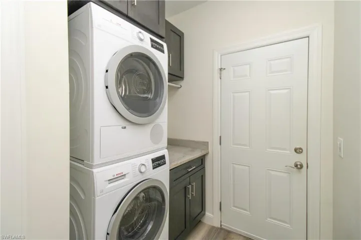 Clothes washing area featuring stacked washer and clothes dryer, light hardwood / wood-style floors, and cabinets
