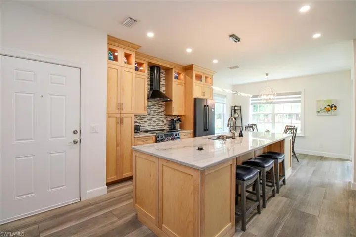 Kitchen with a center island with sink, pendant lighting, black refrigerator, backsplash, and wall chimney range hood