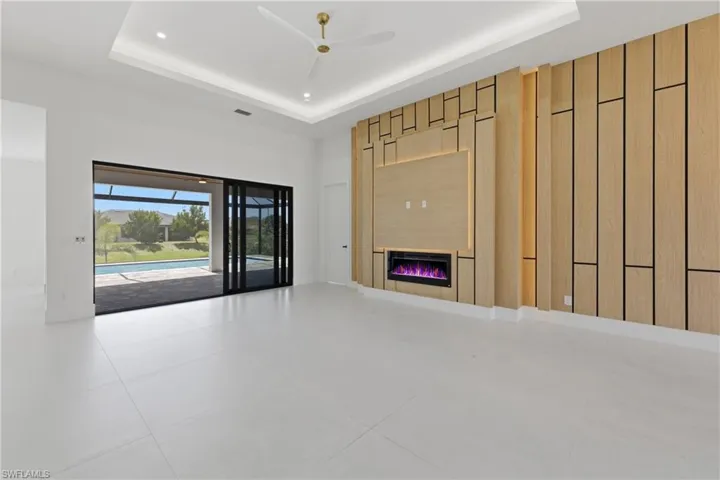Unfurnished living room with a ceiling fan, a glass covered fireplace, a tray ceiling, and a sunroom
