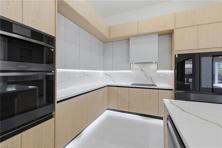 Two tone kitchen featuring modern cabinets, light stone counters, black appliances, tasteful backsplash, and dual tone cabinets