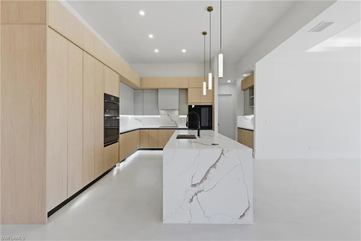 Dual tone kitchen featuring modern cabinets, light stone counters, dual tone cabinetry, and decorative backsplash