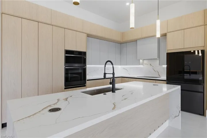 Kitchen with light stone countertops, pendant lighting, two tone color scheme, a warm lit fireplace, and a center island with sink