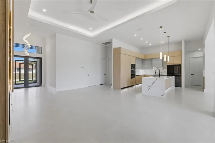 Kitchen with modern cabinets, a kitchen island with sink, hanging light fixtures, open floor plan, and a high ceiling