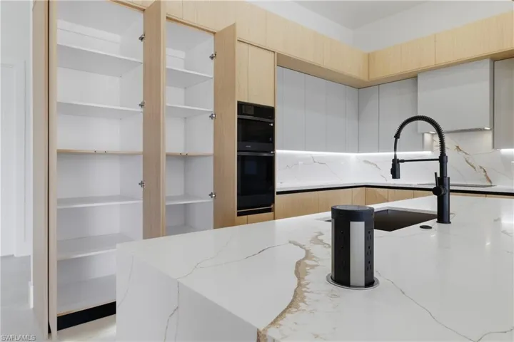 Dual tone kitchen with black appliances, modern cabinets, light stone countertops, range hood, and two tone cabinets