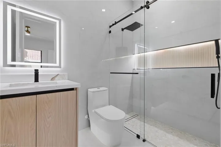 Bathroom with vanity, a marble finish shower, and tile walls