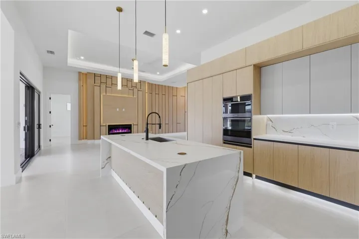 Two tone kitchen with a center island with sink, hanging light fixtures, light stone counters, modern cabinets, and decorative backsplash