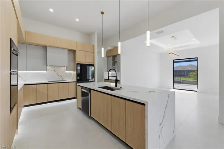 Kitchen featuring light wood finish cabinets, modern cabinets, light stone counters, hanging light fixtures, and a center island with sink