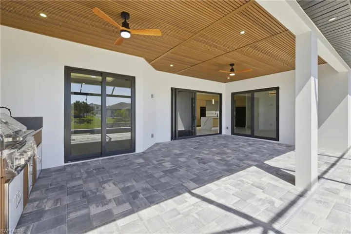 Outdoor pool featuring a sunroom, an outdoor kitchen, a patio, a lawn, and glass enclosure