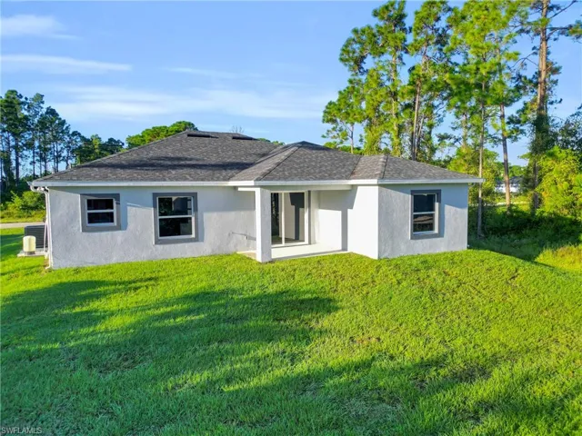 Rear view of house with stucco siding, a yard, a shingled roof, and a patio area