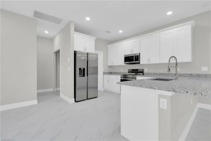 Kitchen with stainless steel appliances, light stone counters, a peninsula, light marble finish floors, and white cabinets