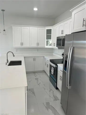 Kitchen with light tile patterned flooring, range, sink, fridge, and light stone countertops