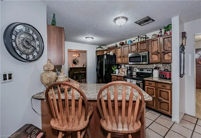 Kitchen featuring kitchen peninsula, stainless steel appliances, decorative backsplash, light tile patterned flooring, and a textured ceiling