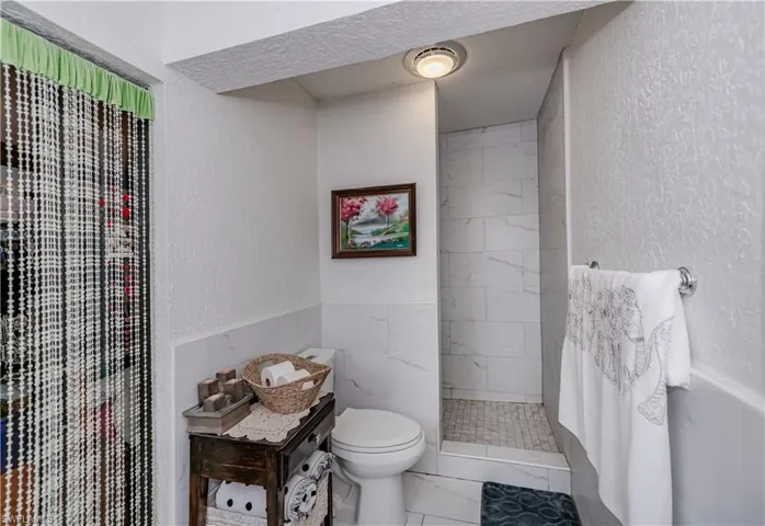 Bathroom with toilet, tile walls, and a tile shower