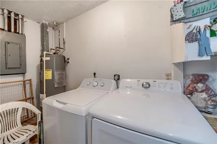Laundry area with washer and clothes dryer, a textured ceiling, electric panel, and water heater