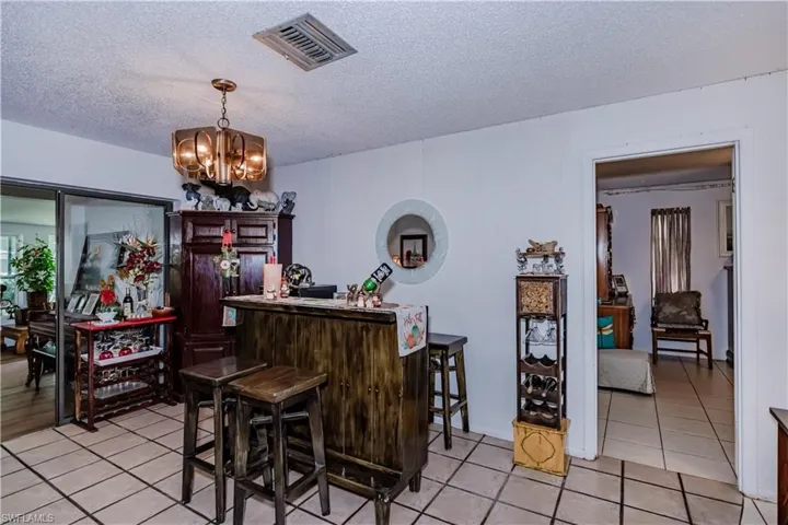 Bar with a textured ceiling, decorative light fixtures, a notable chandelier, light tile patterned floors, and dark brown cabinets
