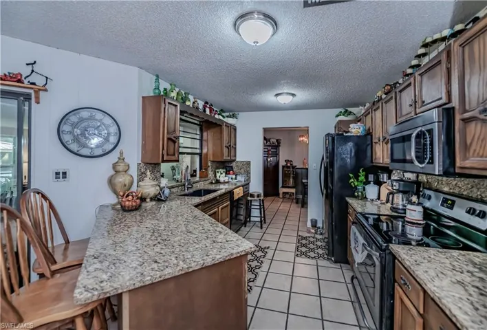 Kitchen featuring black appliances, light tile patterned floors, kitchen peninsula, and sink