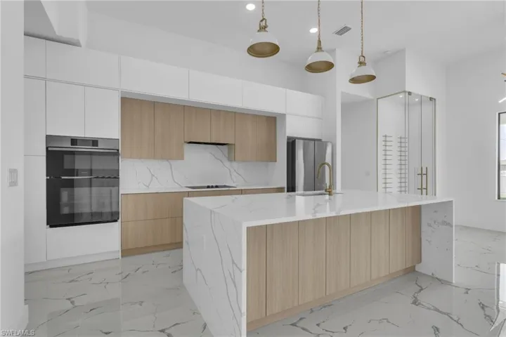 Kitchen featuring hanging light fixtures, light marble finish floors, modern cabinets, light brown cabinetry, and recessed lighting