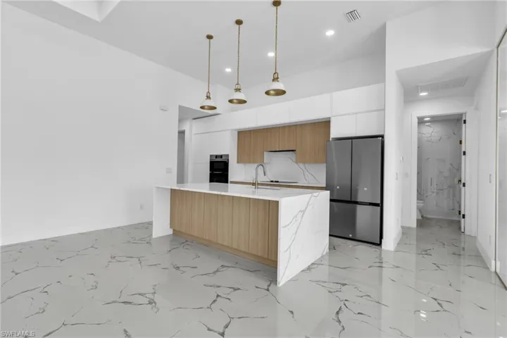 Kitchen featuring appliances with stainless steel finishes, modern cabinets, decorative light fixtures, light marble finish flooring, and recessed lighting