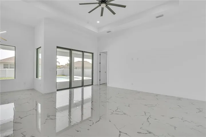 Empty room with light marble finish floors, ceiling fan, a high ceiling, a tray ceiling, and recessed lighting