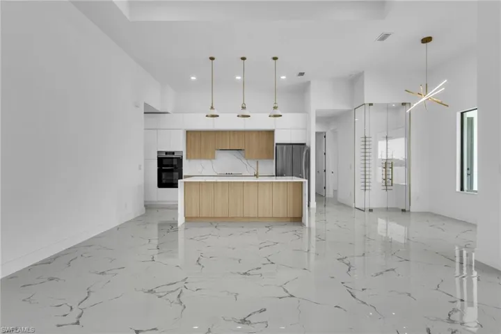 Kitchen featuring modern cabinets, a towering ceiling, pendant lighting, a center island with sink, and light marble finish floors