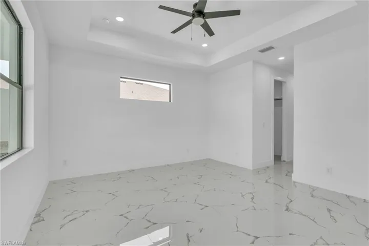 Empty room with recessed lighting, a raised ceiling, light marble finish flooring, and a ceiling fan