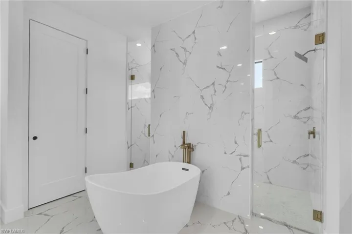 Full bath with a soaking tub, marble tiled flooring, a marble finish shower, and stone wall