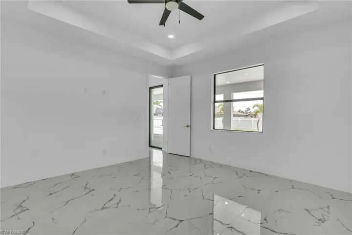 Empty room with a raised ceiling, light marble finish floors, recessed lighting, and a ceiling fan