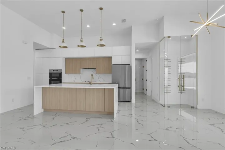 Kitchen with modern cabinets, a center island with sink, hanging light fixtures, appliances with stainless steel finishes, and light stone counters