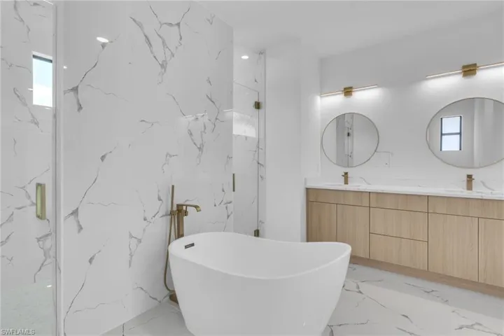 Full bath with a freestanding bath, double vanity, a marble finish shower, light marble finish flooring, and stone wall
