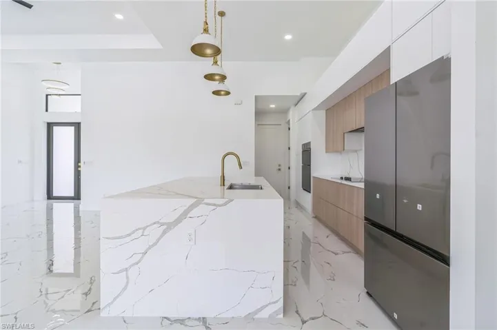 Kitchen featuring modern cabinets, light stone counters, freestanding refrigerator, recessed lighting, and decorative light fixtures