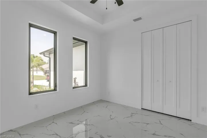 Unfurnished bedroom featuring light marble finish flooring, ceiling fan, and a closet