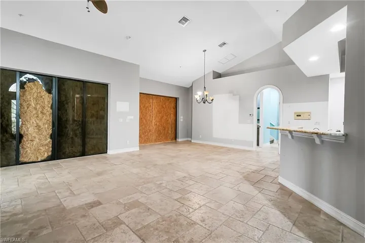 Unfurnished living room with ceiling fan with notable chandelier and lofted ceiling