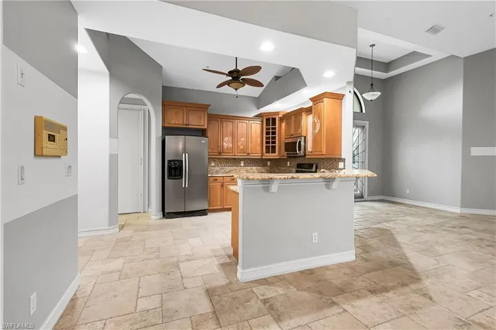 Kitchen featuring decorative backsplash, appliances with stainless steel finishes, light stone counters, a breakfast bar, and ceiling fan