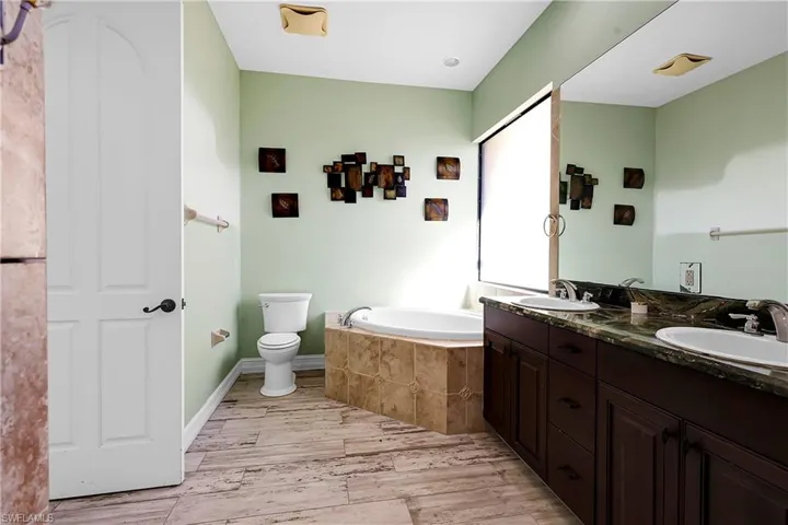 Bathroom featuring hardwood / wood-style floors, vanity, tiled bath, and toilet