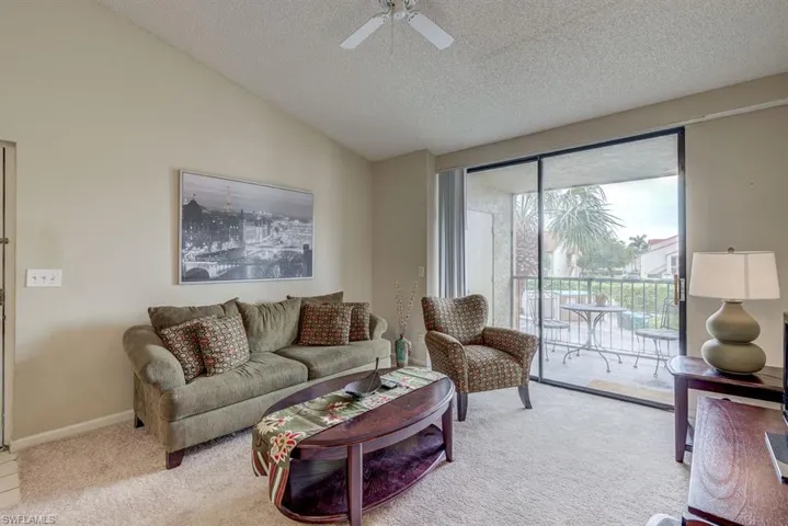 Living area featuring vaulted ceiling, carpet floors, a textured ceiling, and ceiling fan
