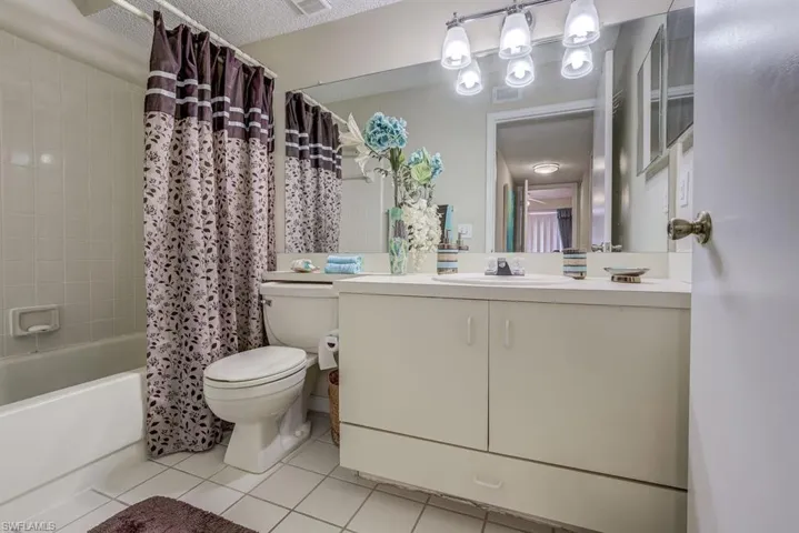Full bath with shower / tub combo with curtain, light tile patterned floors, vanity, and a textured ceiling