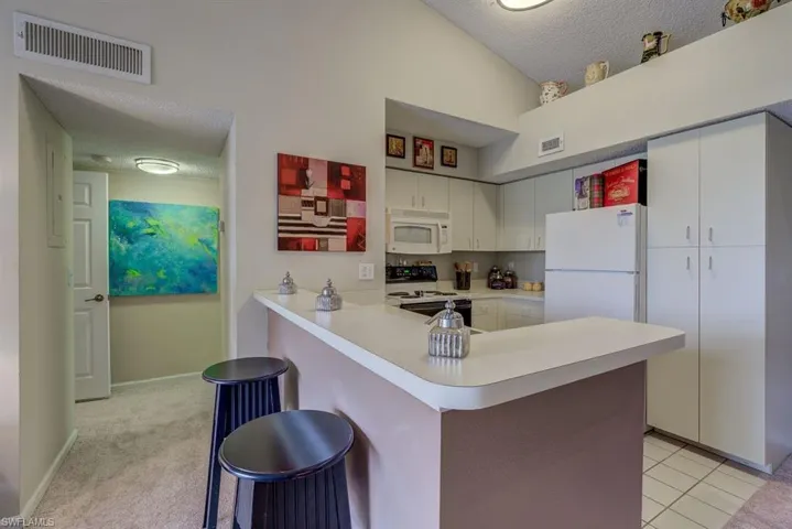 Kitchen with a textured ceiling, a breakfast bar, light countertops, white appliances, and white cabinetry