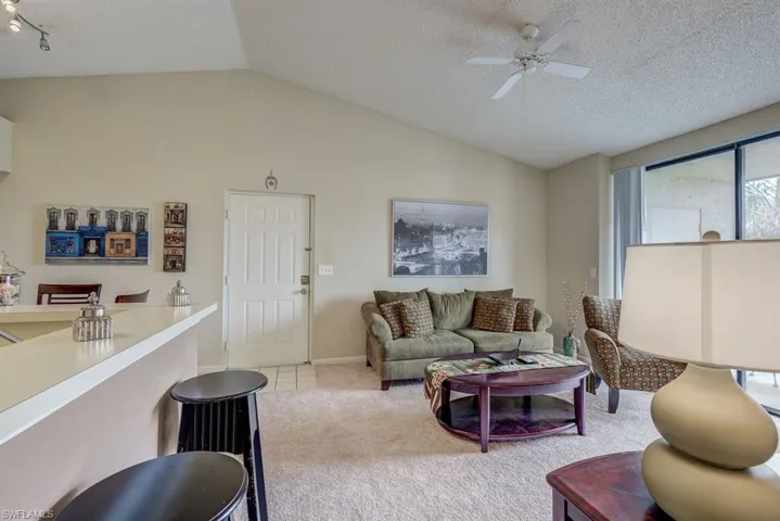 Living area with vaulted ceiling, light carpet, a textured ceiling, ceiling fan, and light tile patterned floors
