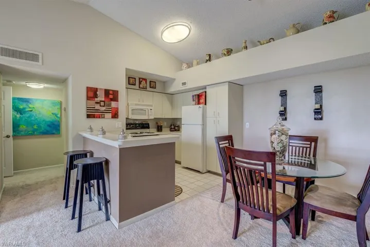 Kitchen with light countertops, a kitchen breakfast bar, white appliances, lofted ceiling, and a peninsula