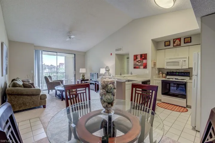 Dining room with vaulted ceiling, light tile patterned floors, a textured ceiling, and ceiling fan