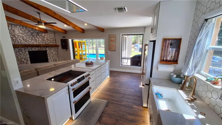 Kitchen with range with two ovens, dark wood finished floors, beam ceiling, white cabinets, and freestanding refrigerator