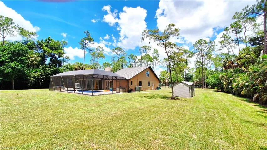 View of green lawn featuring a lanai, a swimming pool, a shed, and view of wooded area
