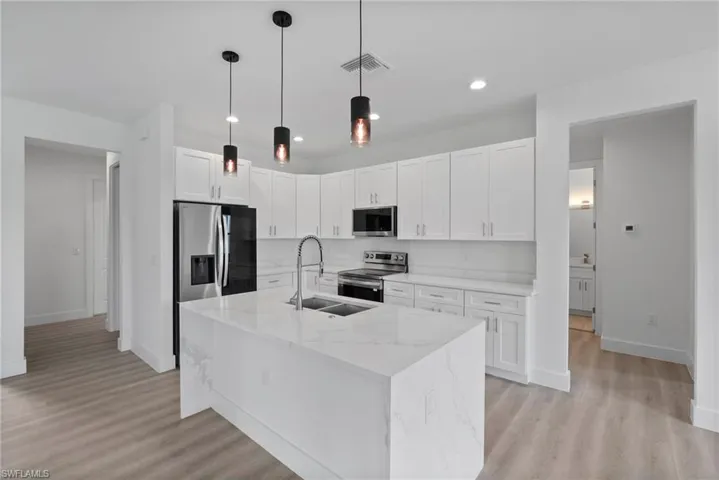 Kitchen featuring appliances with stainless steel finishes, light hardwood / wood-style floors, white cabinetry, light stone counters, and a center island with sink