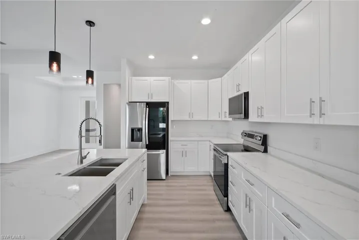 Kitchen featuring light stone counters, hanging light fixtures, white cabinetry, appliances with stainless steel finishes, and light wood-type flooring