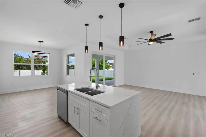 Kitchen with sink, ceiling fan with notable chandelier, white cabinets, light stone countertops, and stainless steel dishwasher