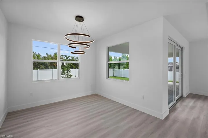 Empty room featuring light wood-type flooring, a notable chandelier, and a wealth of natural light