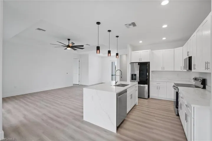 Kitchen with appliances with stainless steel finishes, an island with sink, white cabinets, ceiling fan, and sink