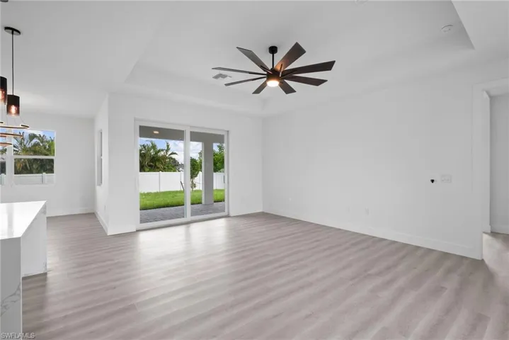 Unfurnished living room featuring ceiling fan, a tray ceiling, and light hardwood / wood-style flooring