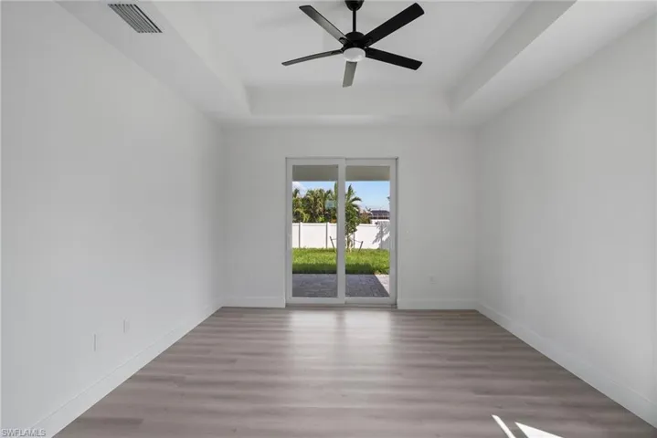 Empty room featuring ceiling fan, light wood-type flooring, and a raised ceiling