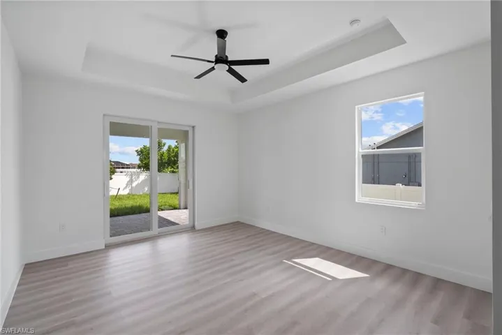 Empty room with a raised ceiling, ceiling fan, and light hardwood / wood-style flooring